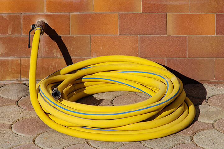 A nicely rolled up garden hose connected to an outside water facucet