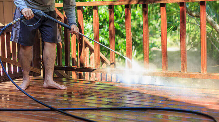 man pressure washing a deck