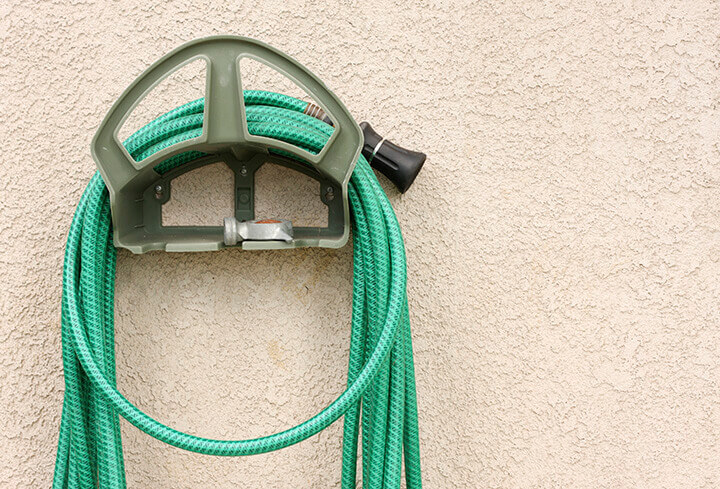 A garden hose and nozzle wound around a wall-mounted reel.