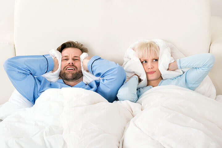 couple in bed covering their ears with pillows