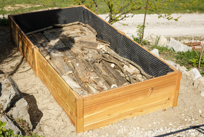 new raised garden bed filled with wood, landscape fabric, and hardware cloth