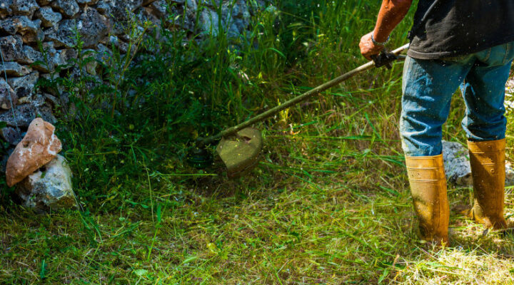 Man using a string trimmer along a stone wall