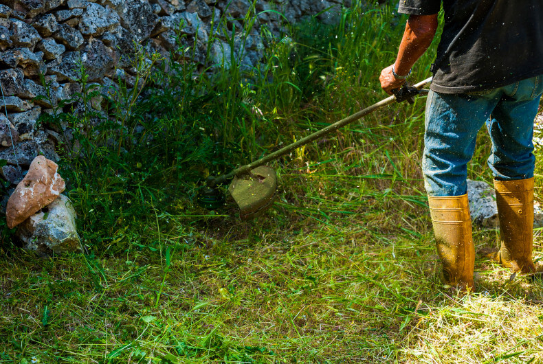 Man using a string trimmer along a stone wall