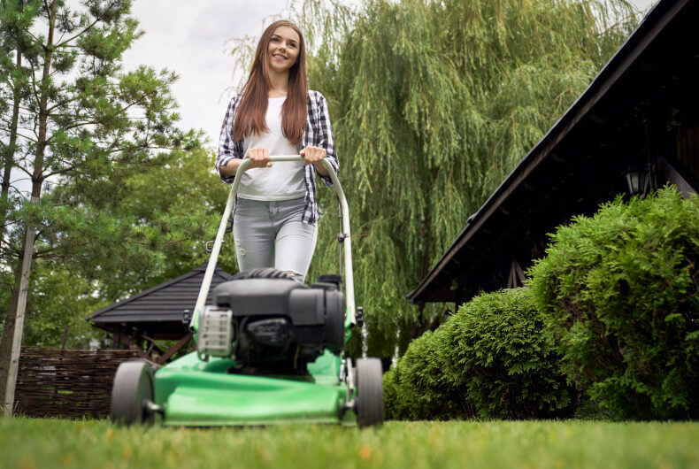 Young woman cutting grass with a lawn mower